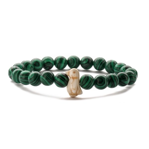 Macro detail of green malachite beads and a white penguin pendant on an elastic bracelet