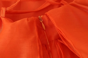Detailed macro view of the seamless invisible zipper on the bright orange chiffon dress