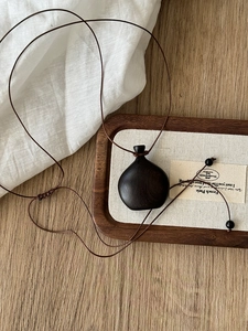 Close-up of wood gourd pendant with adjustable woven rope on a rustic wooden tray