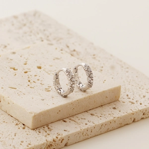 Macro shot of silver S925 earrings with double row zircon pavé on beige stone