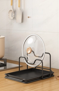 Detail of black metal pot lid holder with dual-slot design and removable drip tray on countertop