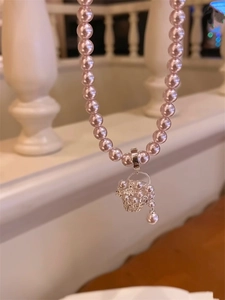 Detail of a pink pearl necklace with a vintage hollow flower basket pendant on white background