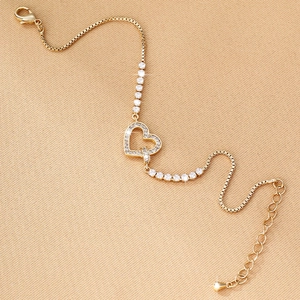 Detail view of a gold heart charm bracelet with sparkling zircons and box chain design