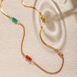 Detail of bohemian gold chain featuring colorful beads in cyan, yellow, and red hues
