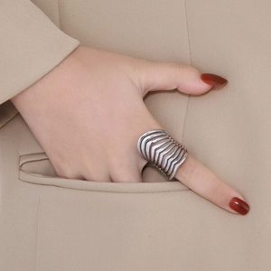 Macro shot of silver wide-band multi-layer hollowed-out ring worn with beige suit