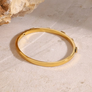 Polished gold stainless steel wide bangle with gear accents and secure clasp