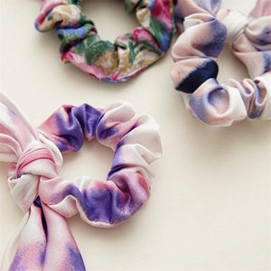Three tie-dye and floral silk satin scrunchies with long ribbons on beige background