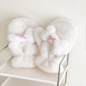 Dettaglio di morbide pantofole bianche di peluche con fiocchi a quadretti rosa su scaffale