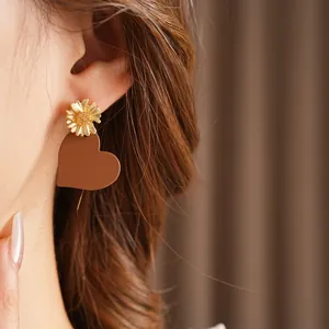 Chic gold daisy stud earrings with matte brown heart pendants worn by model