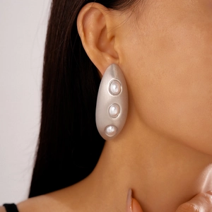 Close-up of geometric matte silver oval earrings with three pearls on a model