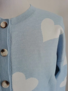 Detail of light blue knit cardigan with white heart patterns and marble buttons
