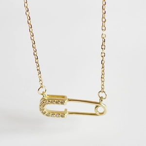 Detailed close-up of golden safety pin pendant with sparkling pave zircon settings