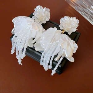 Macro shot of white petal earrings with delicate beaded tassels and golden accents