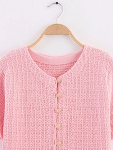 Close-up of pink knit cardigan with embossed texture and gold floral buttons