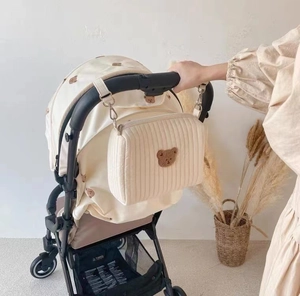 Close-up of quilted beige stroller bag with brown bear embroidery on a handlebar