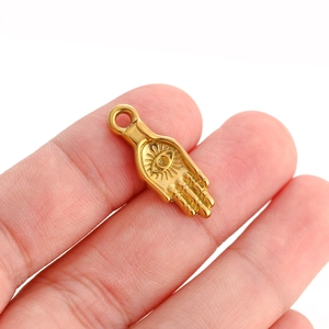 Macro shot of gold Hamsa hand pendant with evil eye detail held on a fingertip