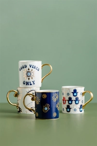 Detail of ceramic mugs with gold handles and blue evil eye patterns on green surface