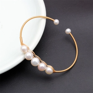 Detailed shot of a gold woven wire bracelet featuring natural freshwater pearls on a tray
