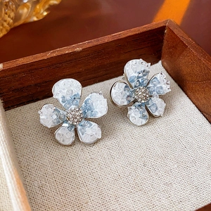 Detail of blue and white gradient crystal flower earrings on beige linen inside a wood box