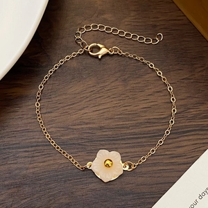 Elegant gold chain bracelet featuring a white shell flower pendant on a dark wood background
