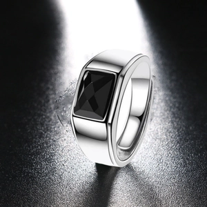 Close-up of a wide silver band ring with a large square black stone on a dark background