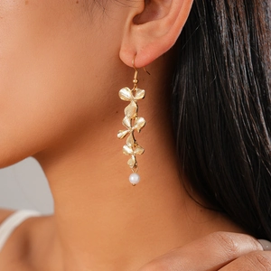 Detail of gold floral tiered earrings with white pearl accents on female model