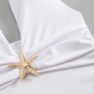 Detail of white swimwear featuring a gold starfish buckle and cross-neck design