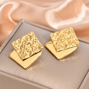 Detailed macro view of golden double-layered geometric square earrings on silk fabric