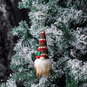 Christmas gnome ornament with red green striped knit hat hanging on a snowy pine branch