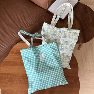 Detail of green plaid floral and elephant print canvas tote bags on a wooden table