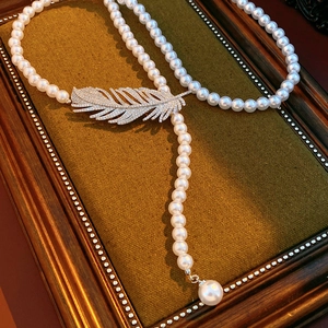 Macro shot of pearl Y-necklace featuring a shimmering zircon-encrusted feather pendant