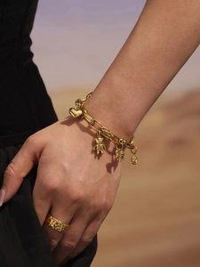 Detailed view of gold multi-charm bear bracelet and hammered metal ring on hand