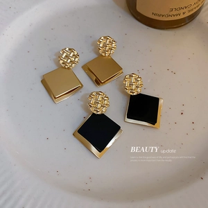 Geometric square sequin metal earrings in gold and black on a ceramic plate