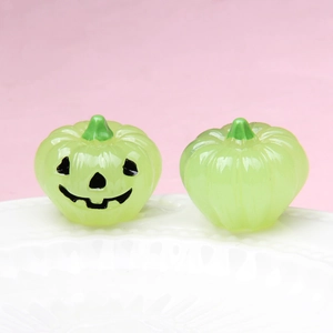 Close-up of light green glowing pumpkin charms with carved smiles on a white plate