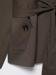 Detailaufnahme des dunkelbraunen Trenchcoat-Stoffs mit Marmorknöpfen und Gürtel