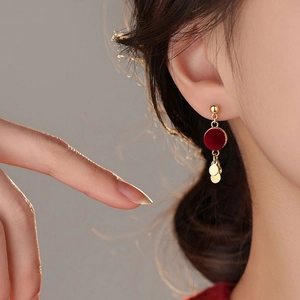 Elegant gold earrings with red flocked discs and dangling metal charms on a female model