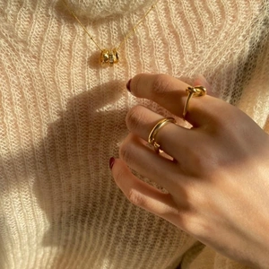 Close-up of gold 925 silver necklace with zircon pendant and rings on beige knitwear