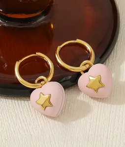Macro shot of pink heart earrings with gold stars on a textured white background