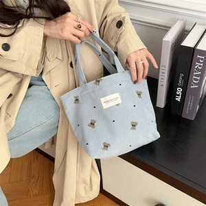 Detail of light blue corduroy handbag with embroidered teddy bear and white woven label