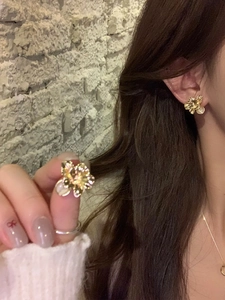 Close-up of golden flower stud earrings with cat eye stones and pearls on a model