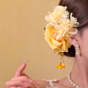 Detail of yellow fabric rose hair clip with elegant metal tassels and pearl accents