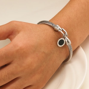 Macro shot of silver twisted cable bangle with Roman numeral disc charm on a model's wrist