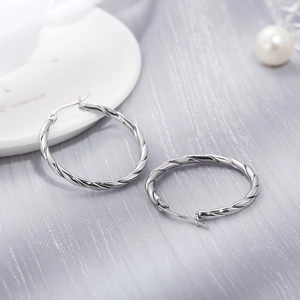 Macro view of 30mm twisted rope hoop earrings in silver on elegant silk fabric