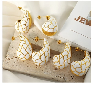 Détail macro de boucles d'oreilles goutte avec émail blanc et motif girafe doré