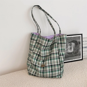 Detail of green and white checkered canvas tote bag with purple lining and logo plaque