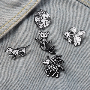 Dunkle Emaille-Pins mit Skeletten von Katzen und Einhörnern auf blauem Denim-Stoff