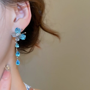 Detail of butterfly drop earrings with blue crystals and silver fringe on a model