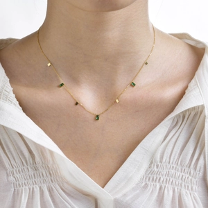 Detail of gold chain necklace featuring rectangle green zircon gems on a model
