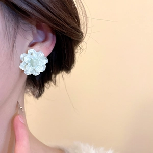 Close-up of white 3D flower stud earrings with pearlescent finish on model ear