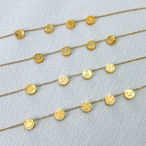 Collana a catena dorata con ciondoli incisi come smileys e cuori su sfondo bianco
